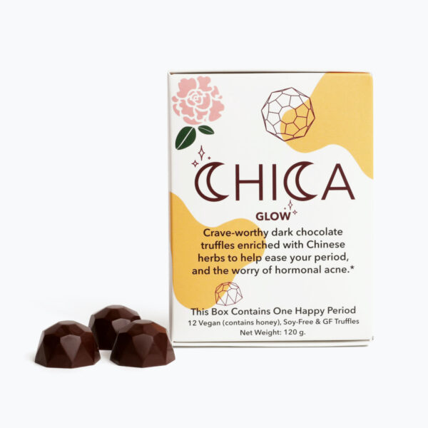 A box of Chica Glow stands in front of a white background, with three Chica Glow truffles grouped to the left of the box. The Chica Glow box says, "Crave-worthy dark chocolate truffles enriched with Chinese herbs to help ease your period, and the worry of hormonal acne.* This box contains one happy period. 12 Vegan (but, contains honey), Soy-Free, and Gluten Free truffles.
